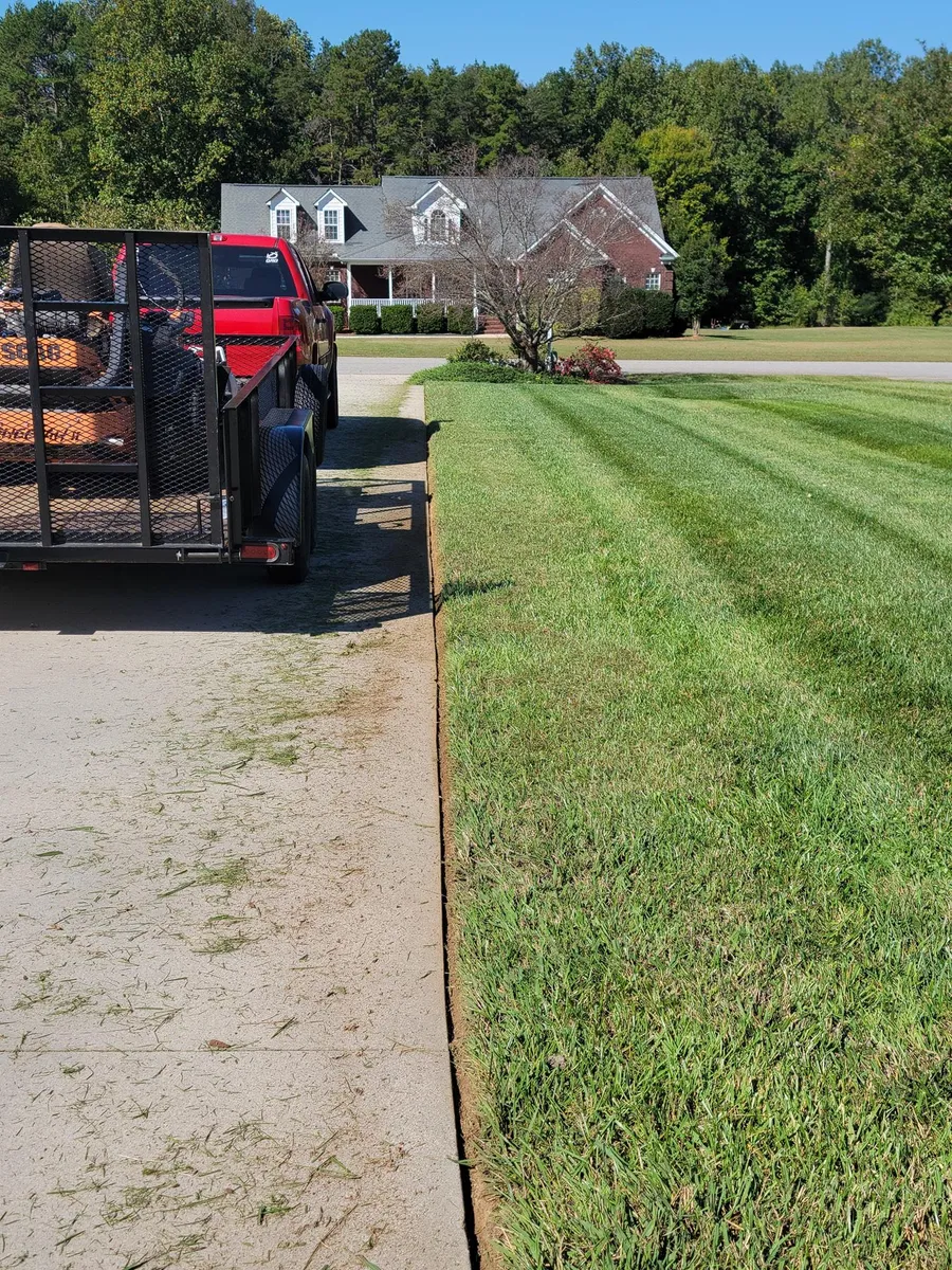 Pickup truck and trailer parked beside a freshly mowed lawn